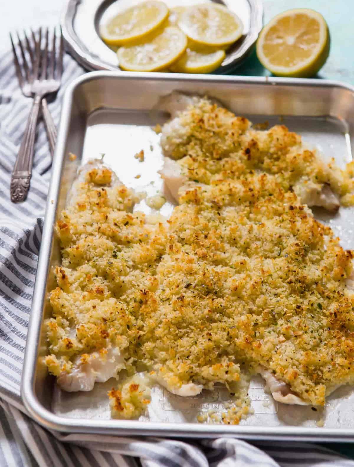 Crispy baked haddock on a sheet pan with two forks and lemon slices in background