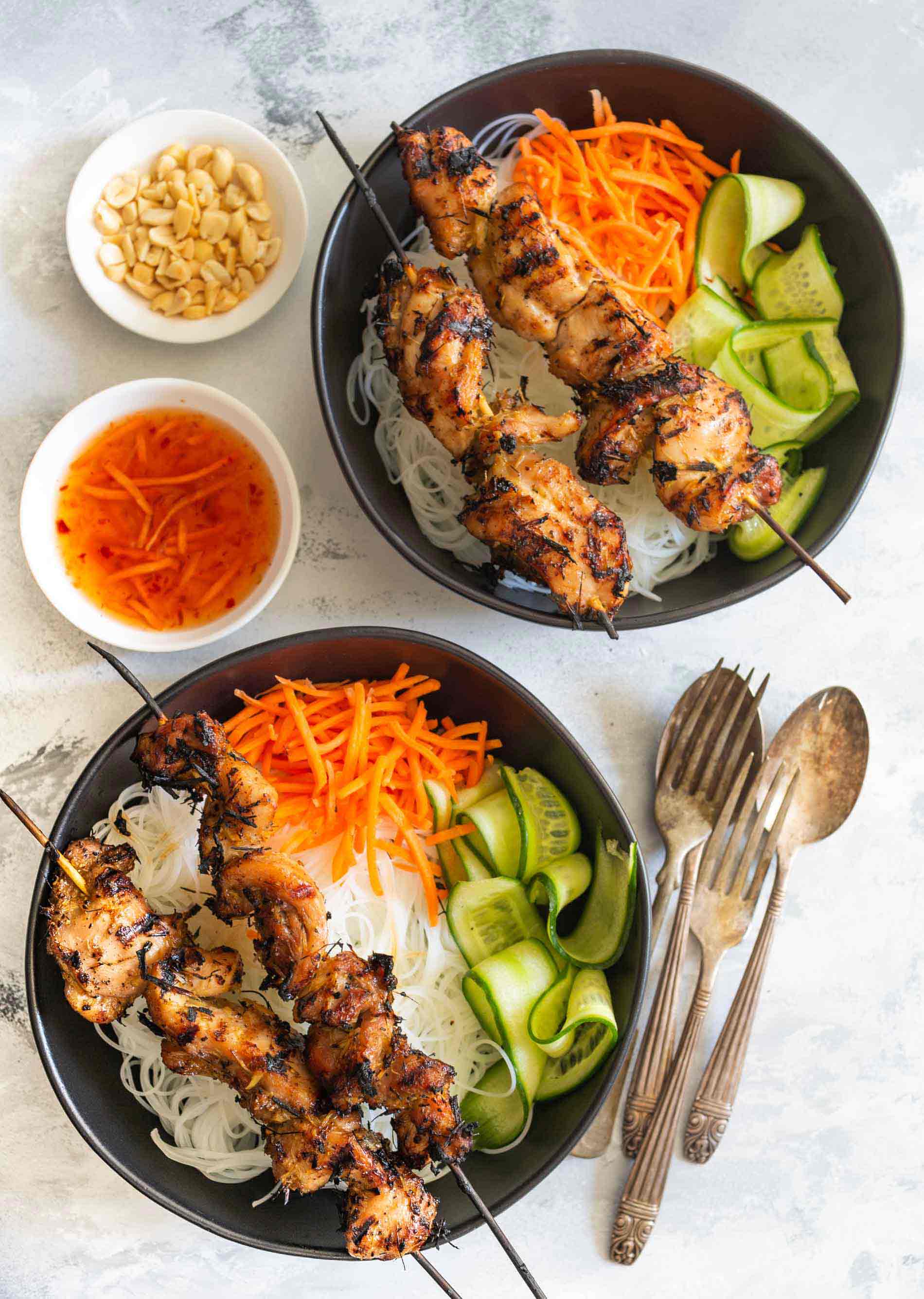 Overhead shot of lemongrass chicken skewers set on top of rice noodle bowls with fresh vegetables