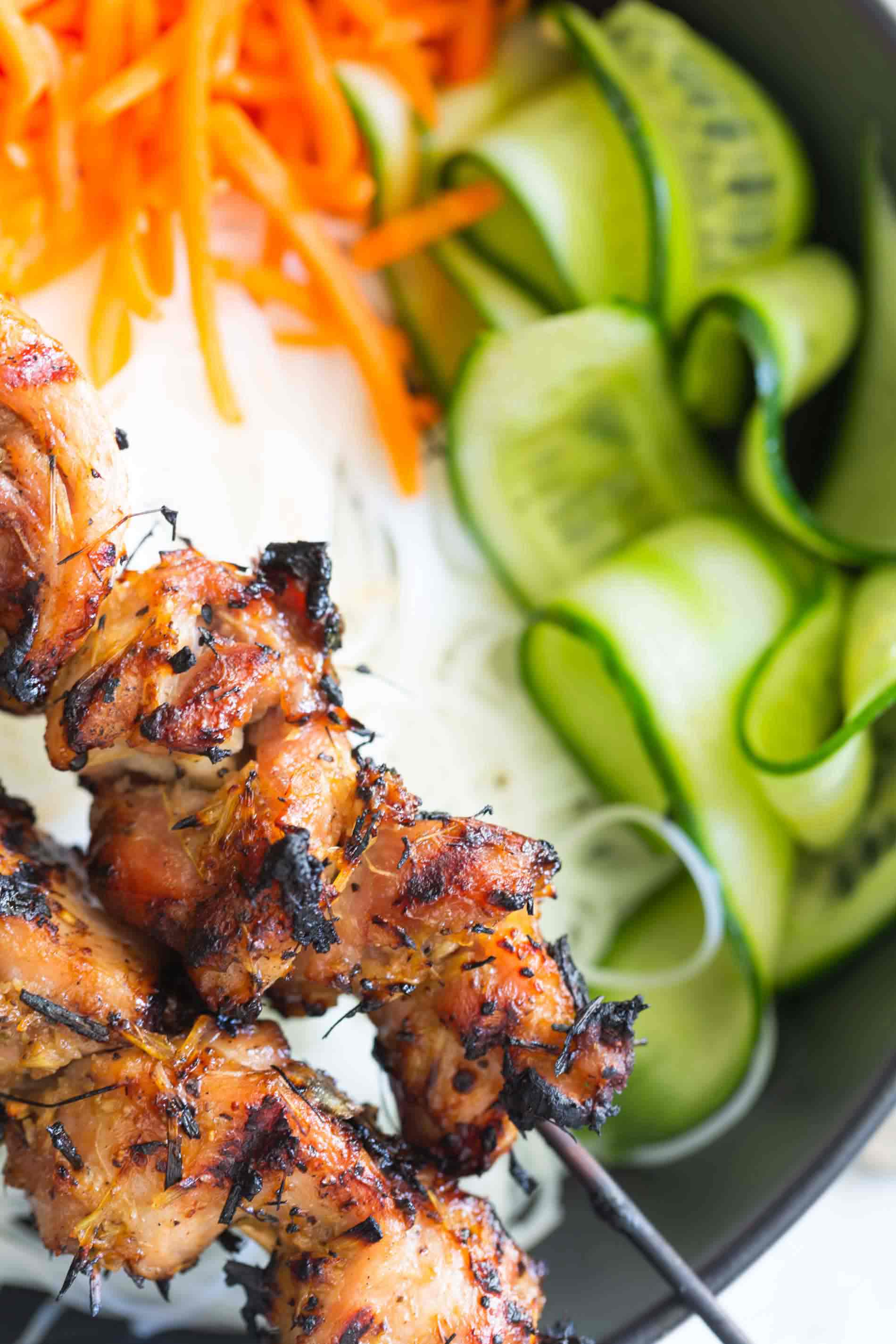 Closeup shot of lemongrass chicken skewers set atop rice noodle bowls