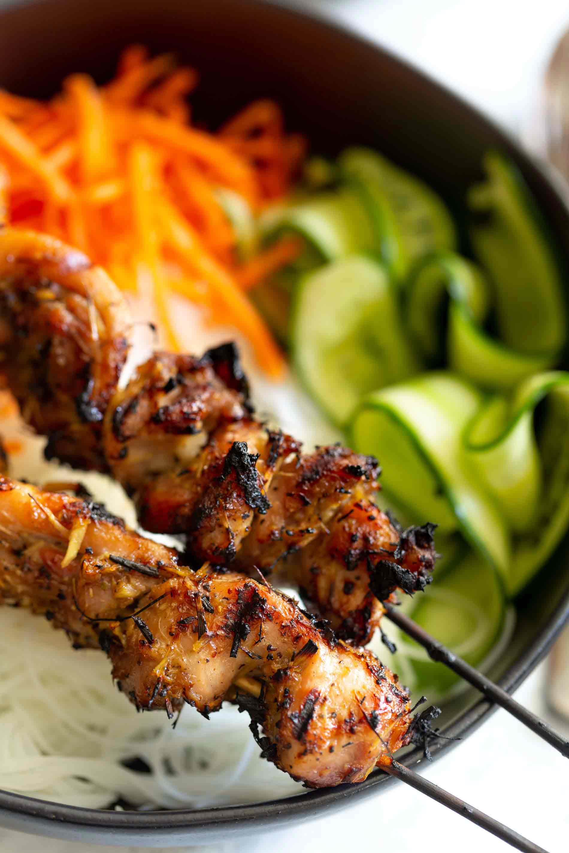 Close up shot of 2 lemongrass chicken skewers on top of rice noodle bowl with veggies