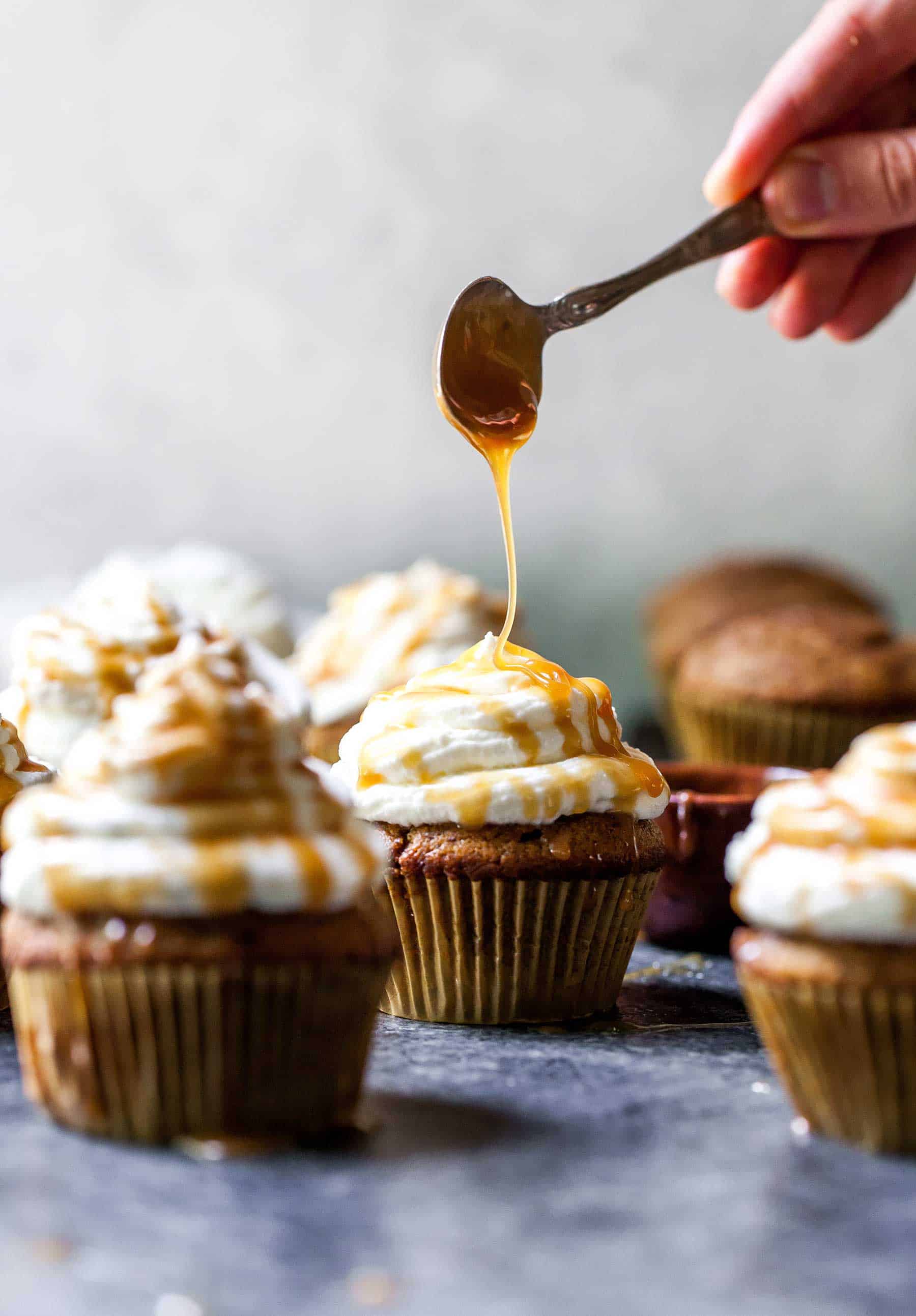 Caramel sauce being drizzled over the tops of pumpkin spice latte cupcakes.