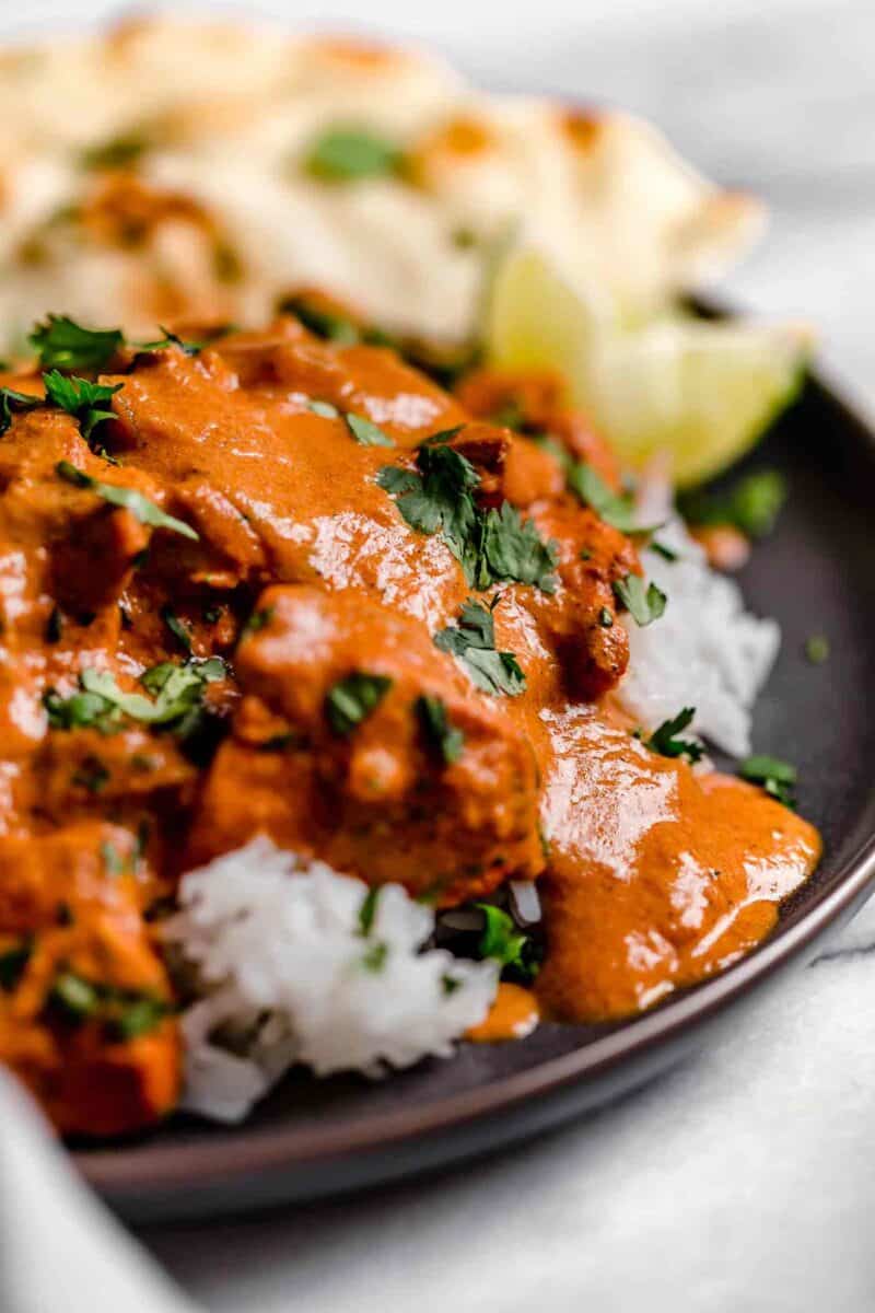 An up close photo of the chicken tikka masala with white rice on a dark brown plate.