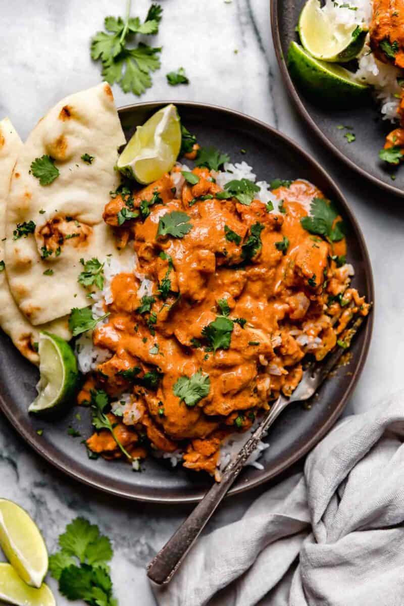 slow cooker chicken tikka masala on a dark brown plate with white rice and naan. a fork can be seen on the side in the rice covered with the curry.