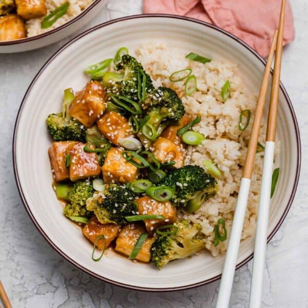 Overhead view of a teriyaki tofu bowl with broccoli, with a pair of chopsticks resting on the edge of the bowl.