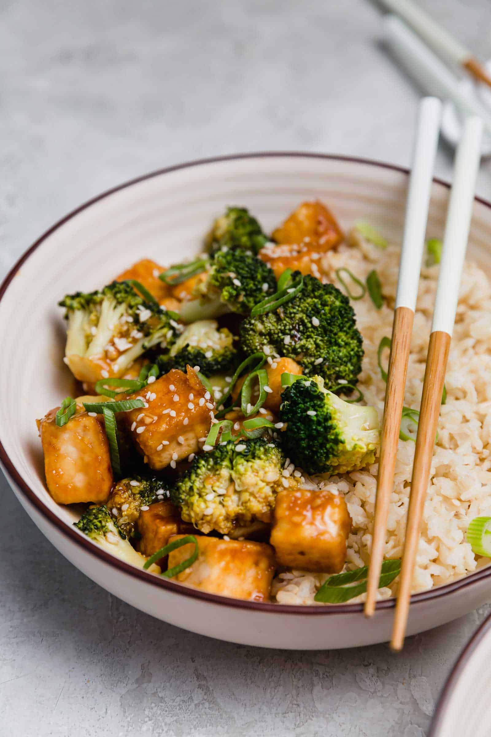 Close up of a teriyaki tofu and broccoli bowl with a set of chopsticks.