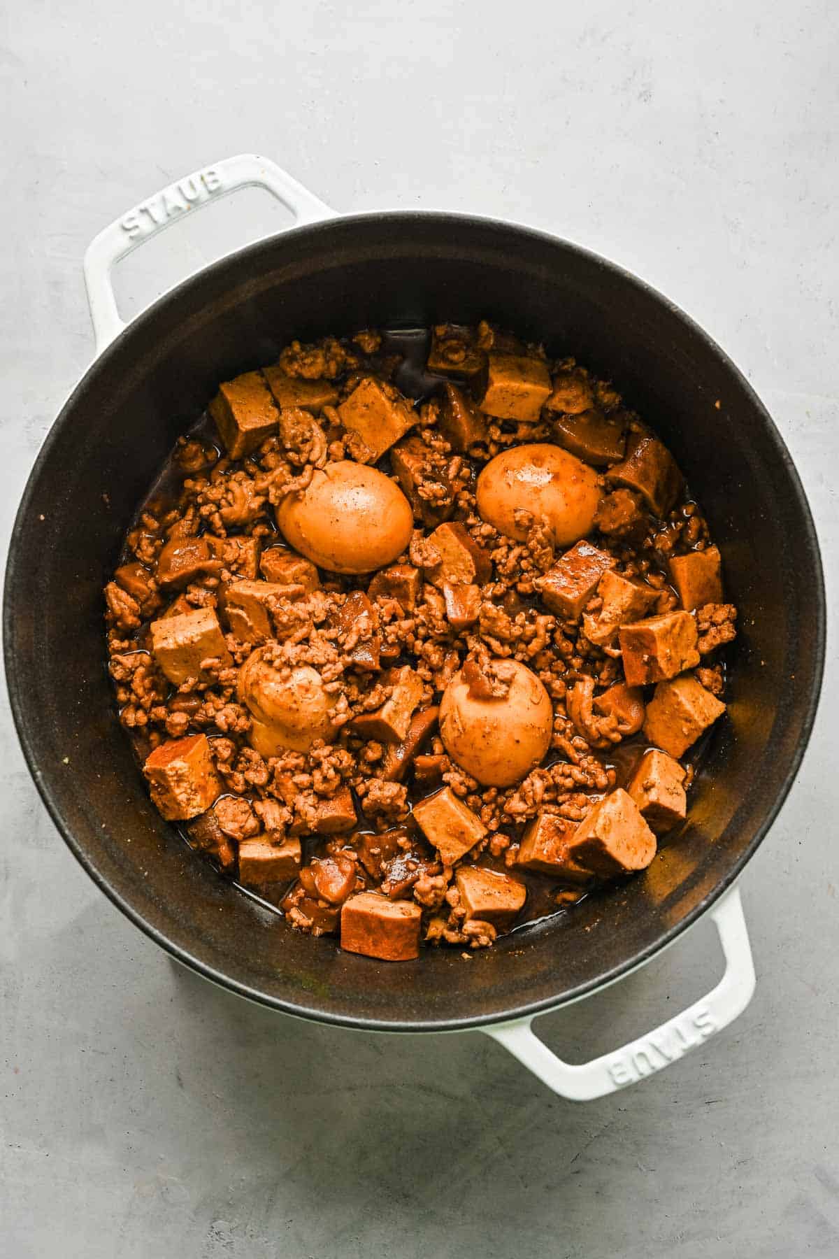 Overhead view of braised minced pork in a pot with eggs, mushrooms, and tofu.