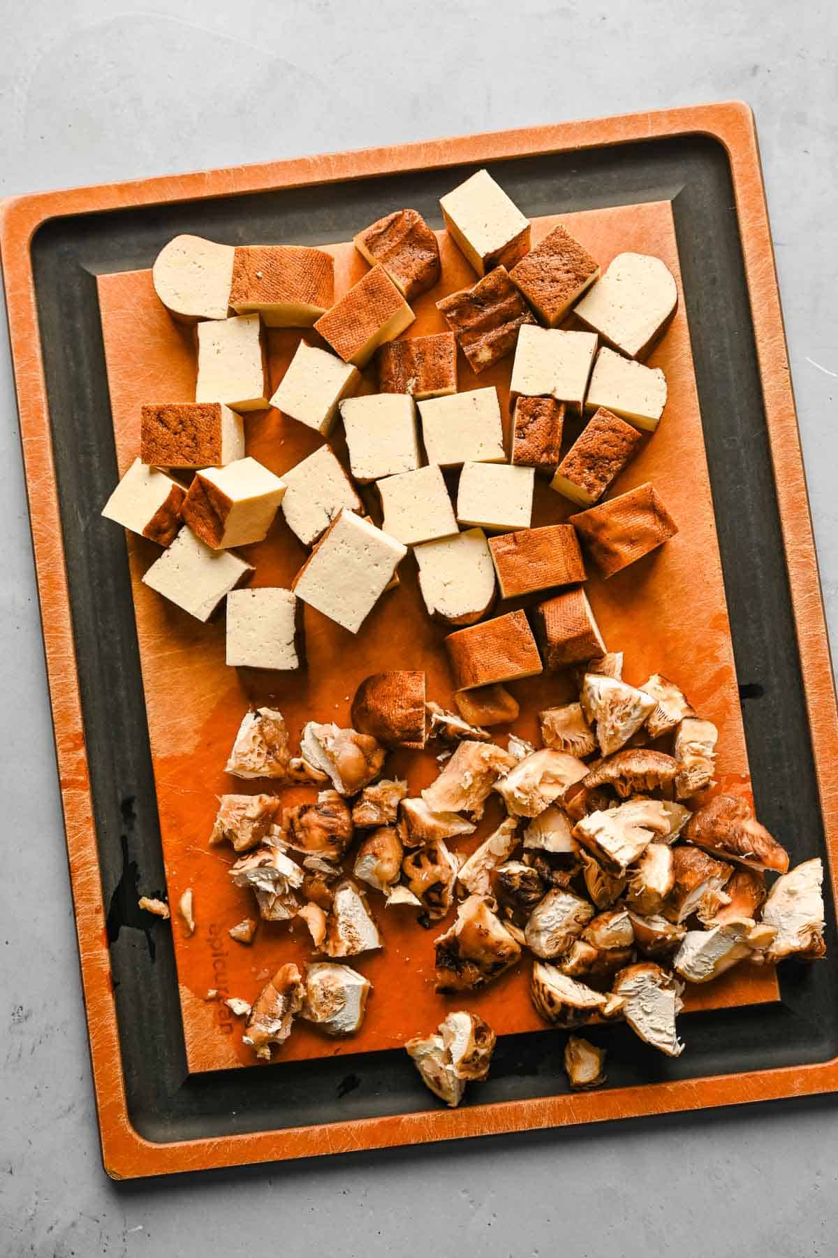Chopped tofu and shiitake mushrooms on a wooden cutting board.