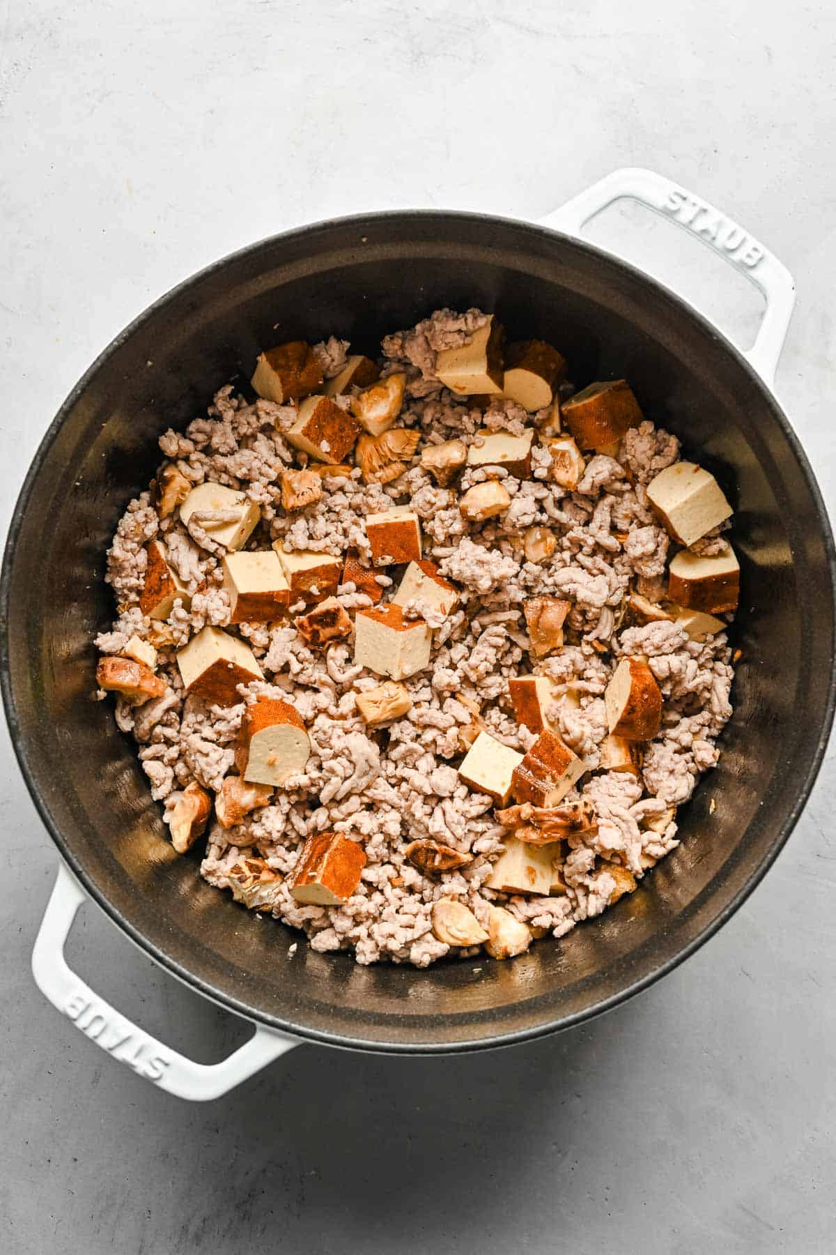 Shiitake mushrooms and tofu added to a pot with braised minced pork.