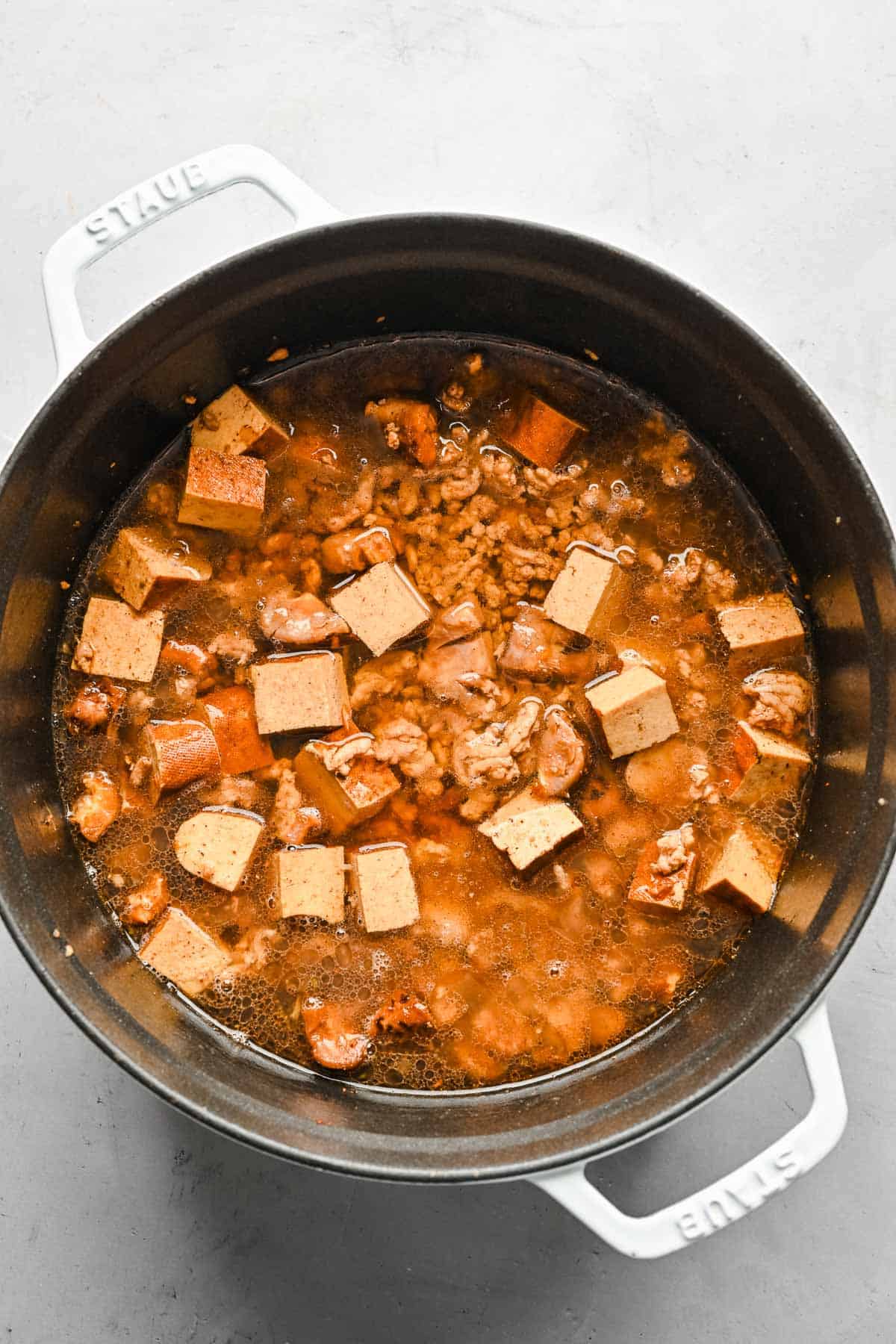 Water added to a pot with braised minced pork, mushrooms, and tofu.