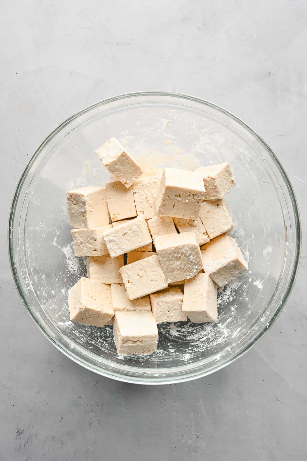 Cubed tofu tossed with cornstarch in a glass bowl.