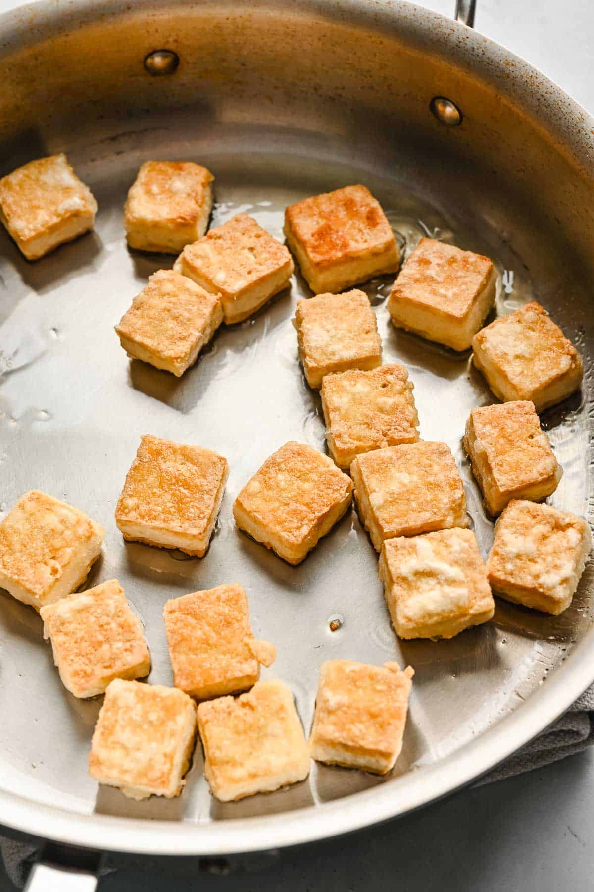Close up of browned cubed tofu in a metal skillet.