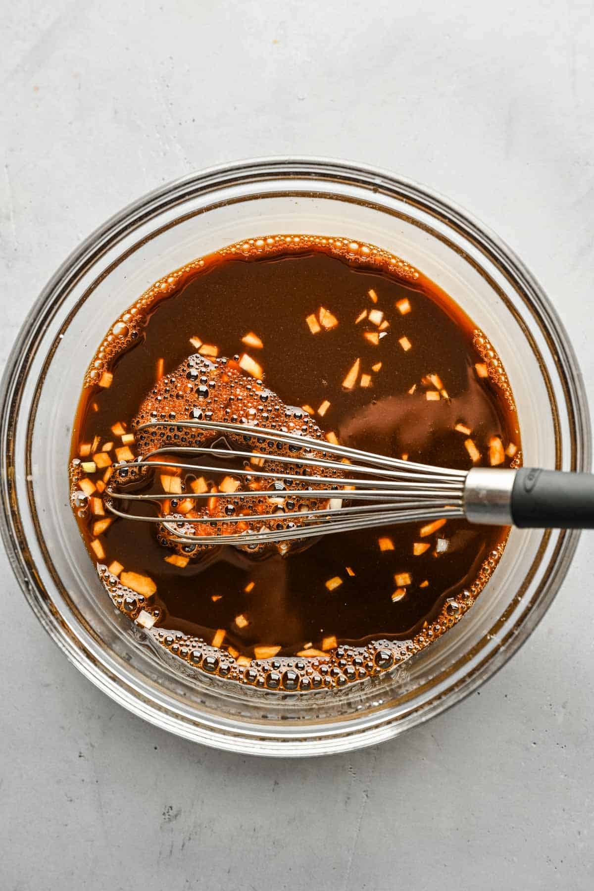 Teriyaki sauce in a glass bowl with a whisk.