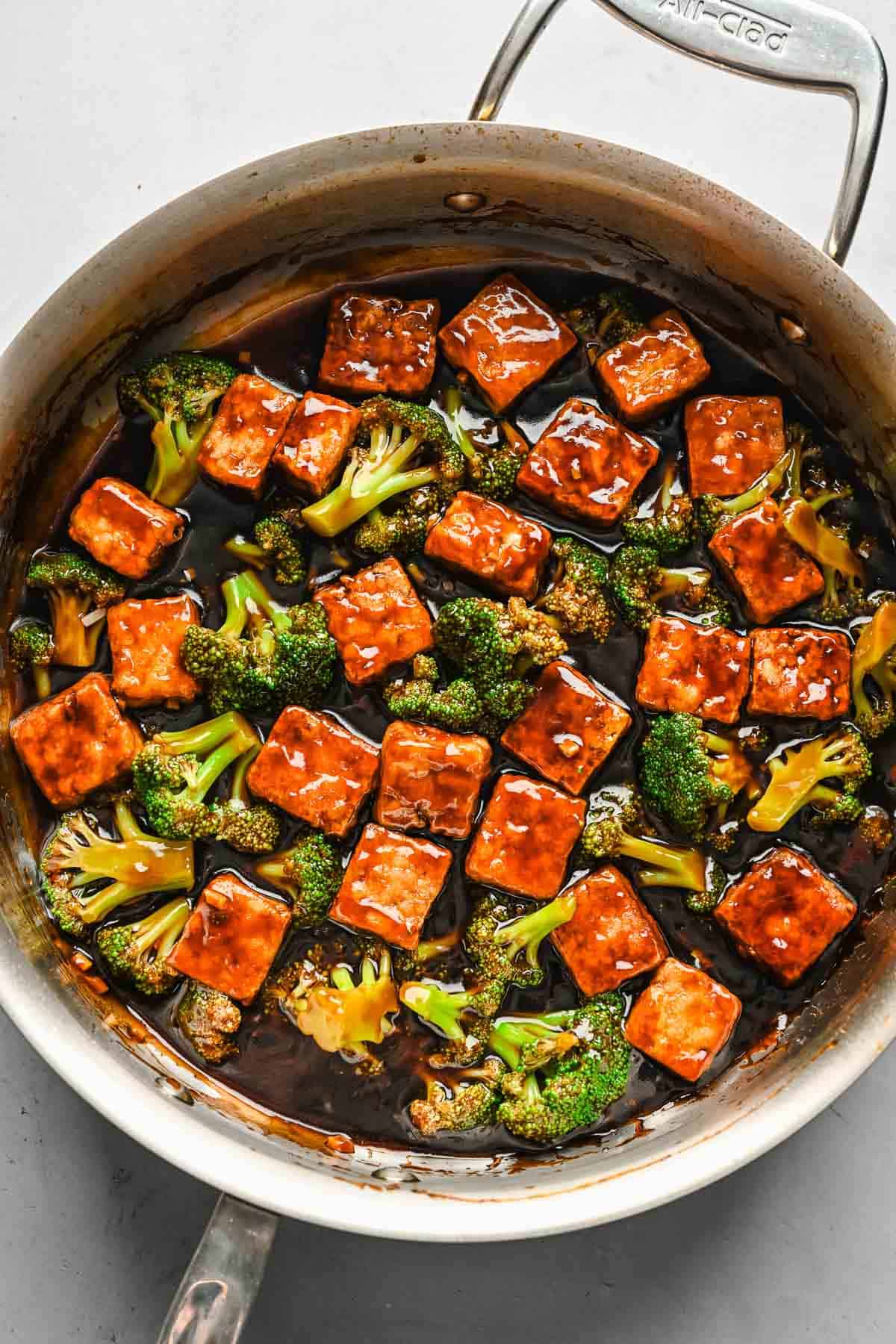 Cubed tofu, broccoli, and teriyaki sauce combined in a skillet.