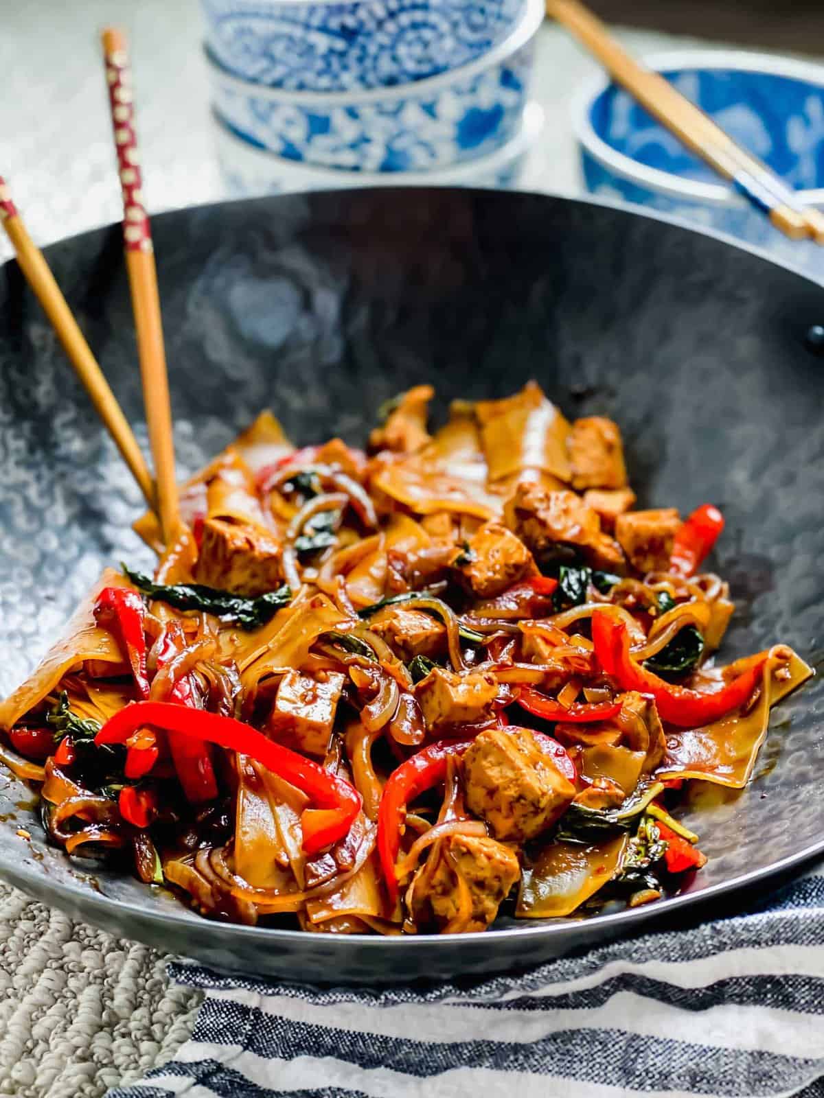 Drunken noodles with tofu in wok with chopsticks.