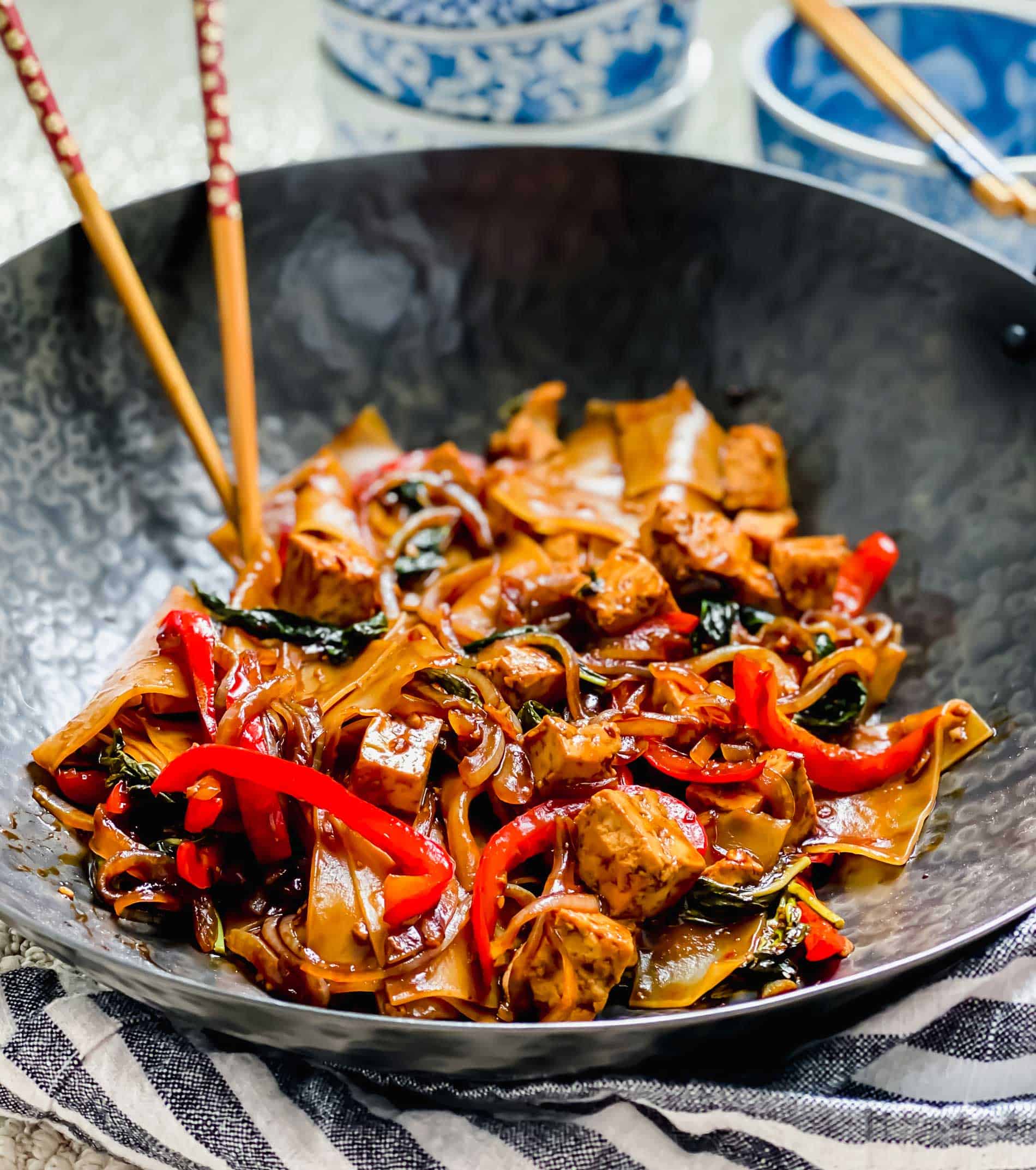 Drunken noodles with tofu in wok with chopsticks.