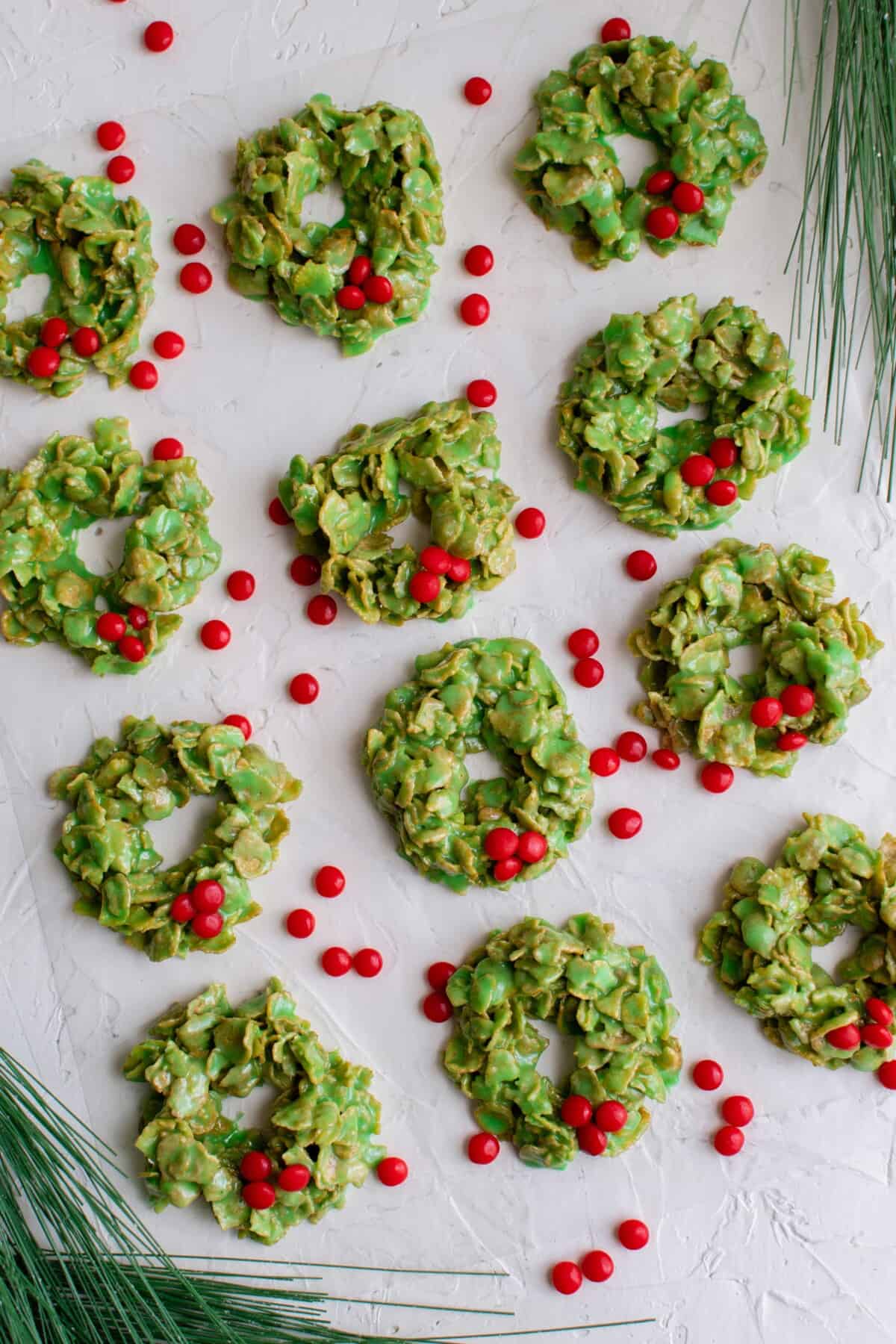 a batch of cornflake cookies are next to scattered red hots candies