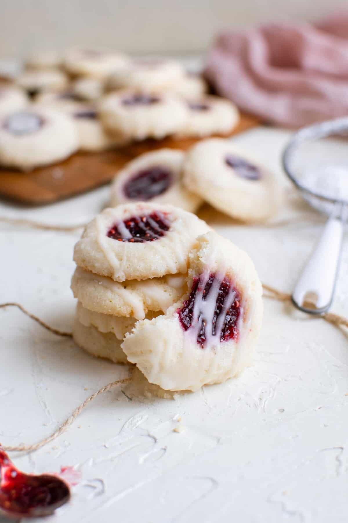 a raspberry thumbprint cookie is bitten in half and set next to a stack of other cookies