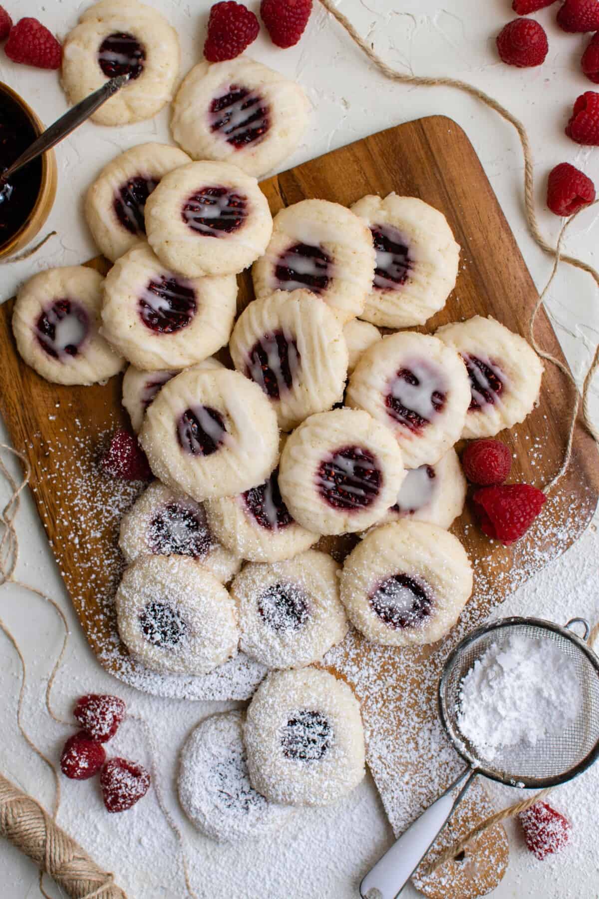 overhead image of raspberry thumbprint cookies on a cutting board with powdered sugar sprinkled on half