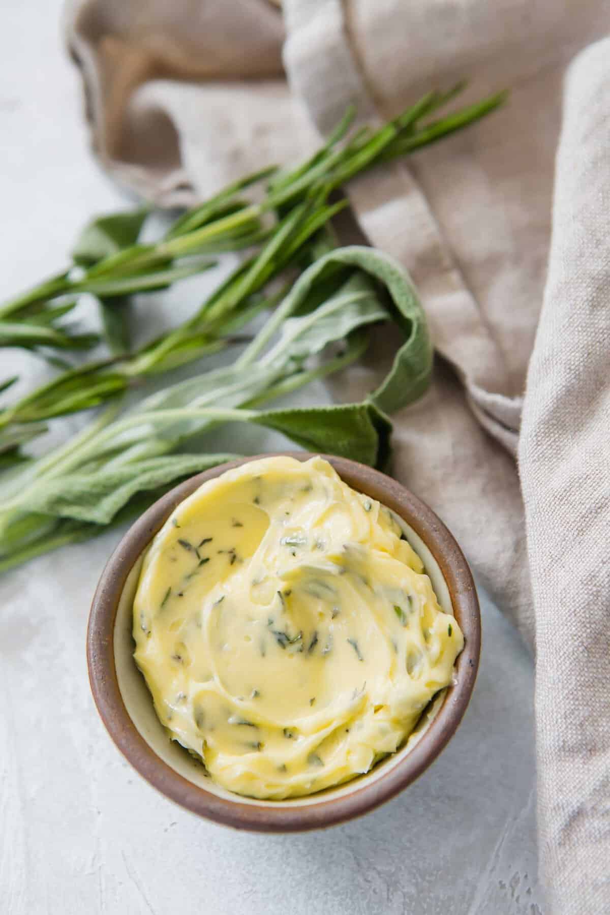 Closeup of small bowl filled with compound butter with sprigs of herbs in background