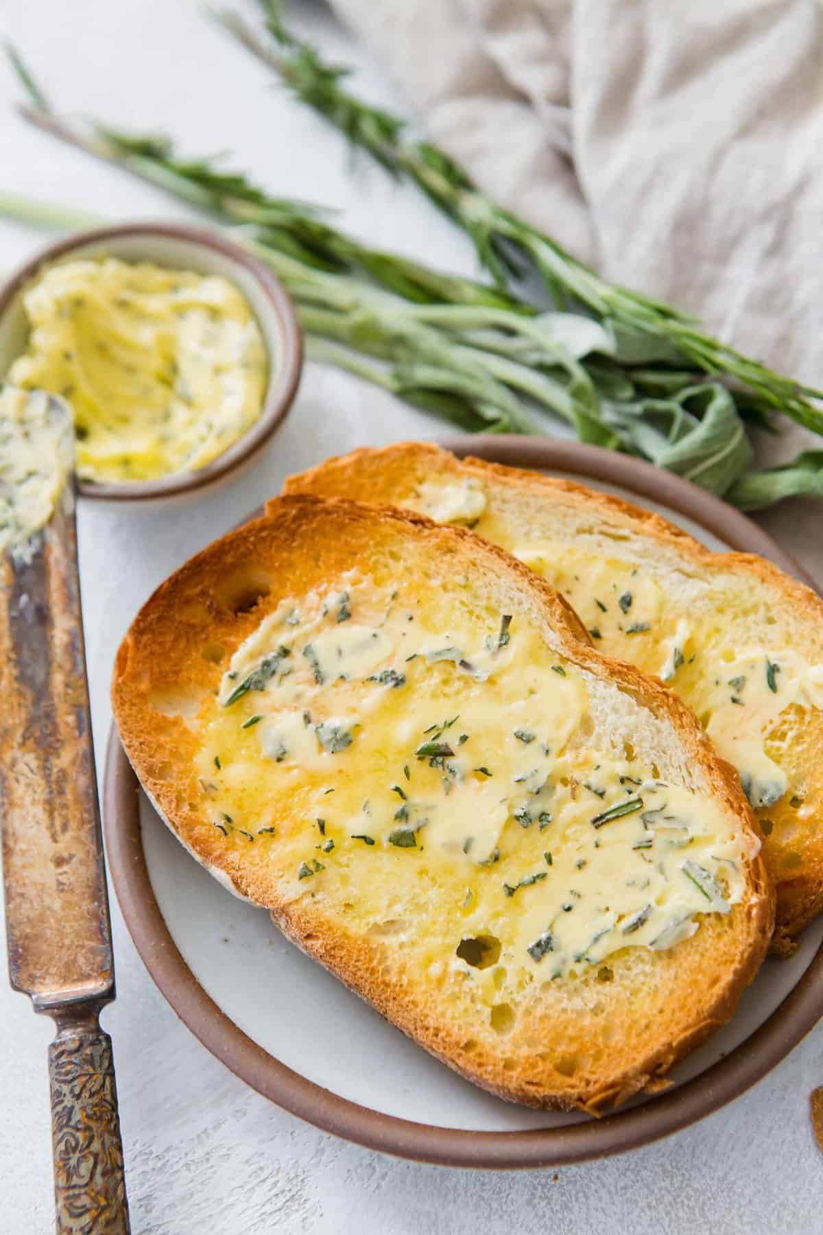 Two pieces of toasted bread on plate topped with melted compound butter.