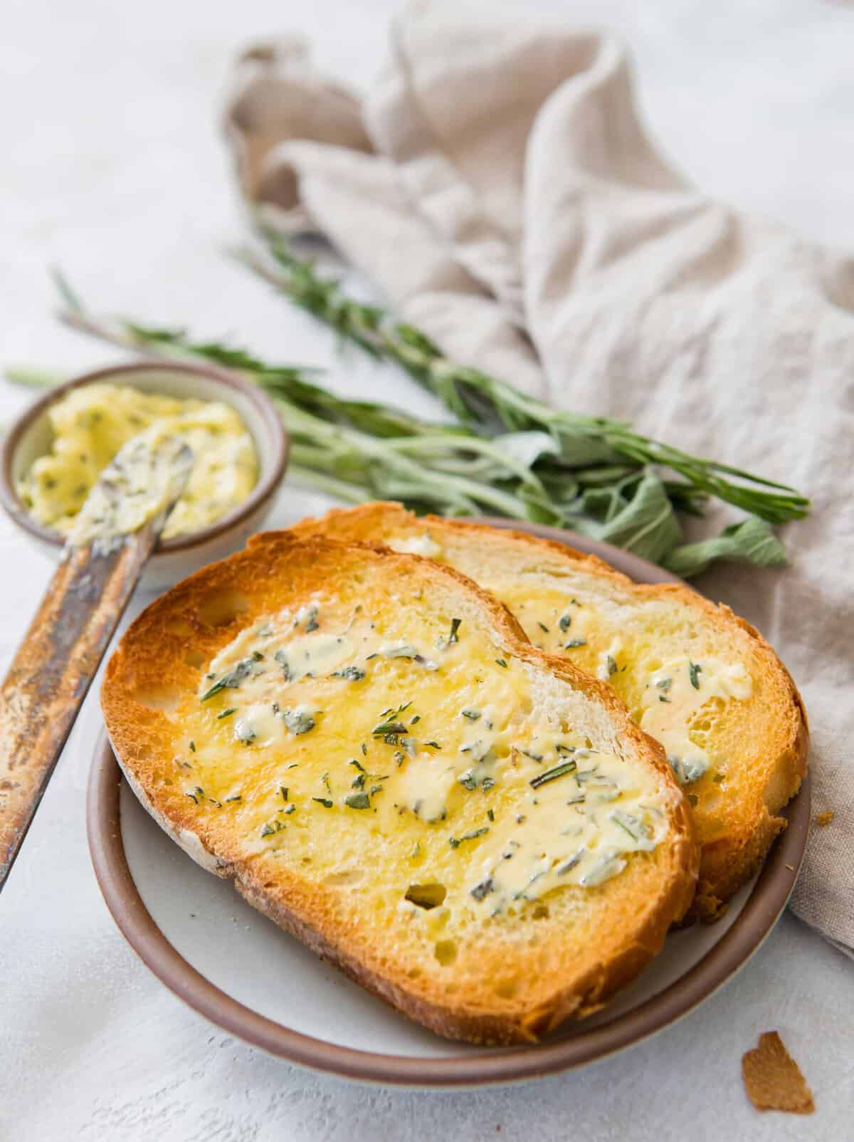 Two pieces of toast topped with melted compound butter on a plate