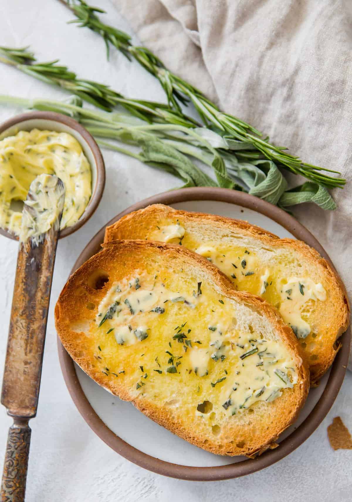 Overhead view of two pieces of toast on plate, each topped with herbed compound butter