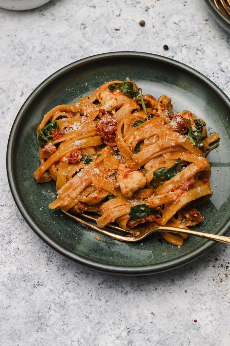 A golden fork is placed slightly under a small serving of pasta in a dark green bowl. 