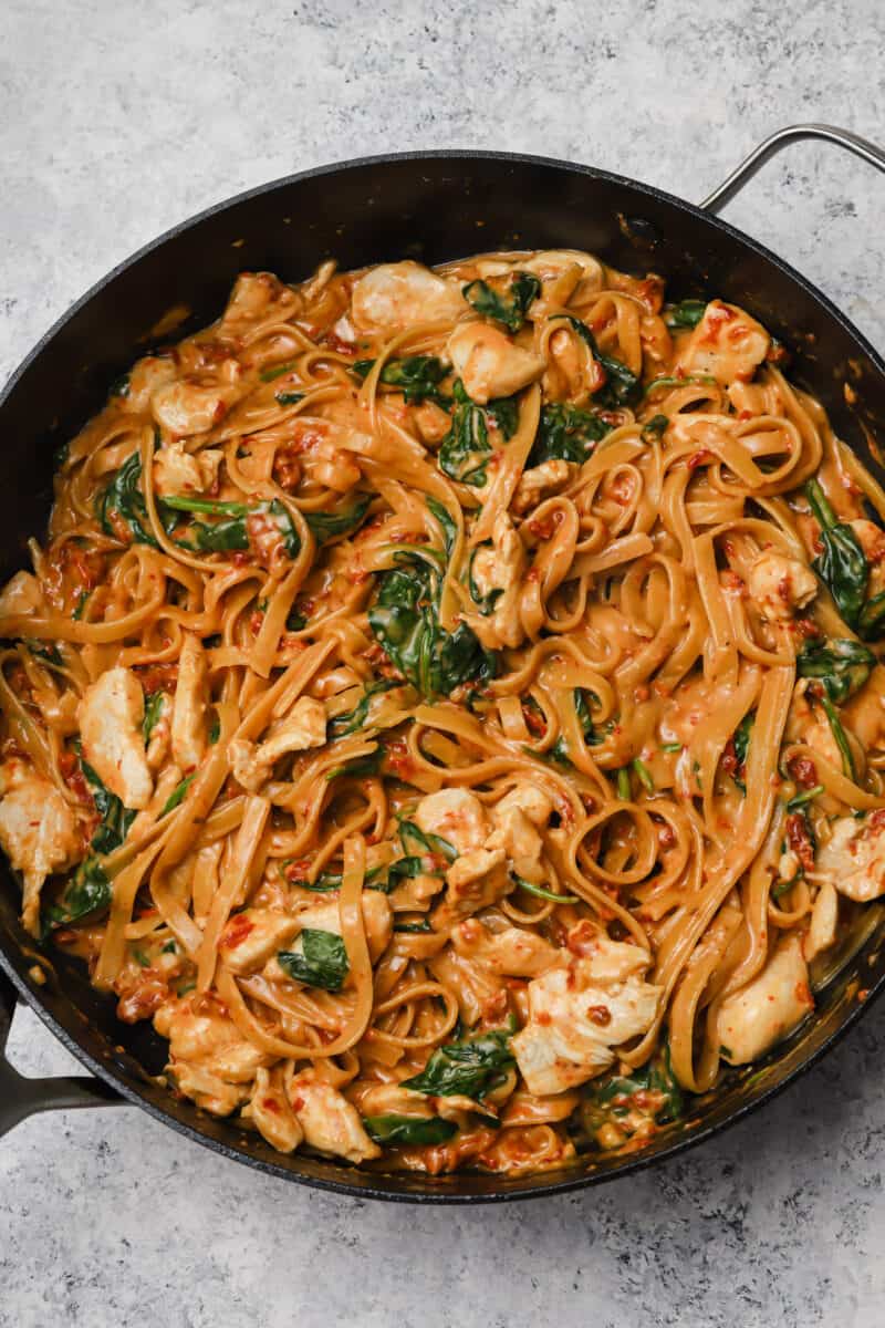A large skillet contains spinach, noodles and white chicken meat, all covered in reddish orange tomato pasta sauce.