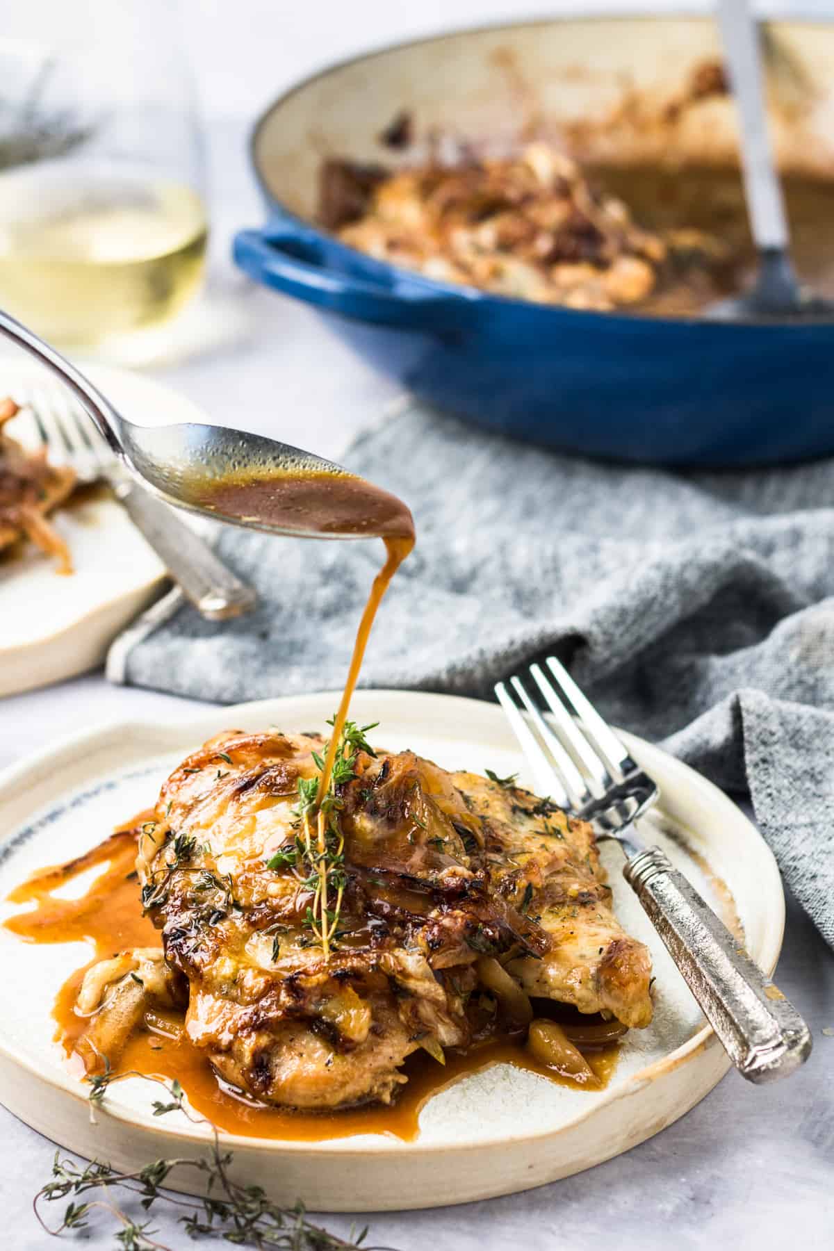 a spoon drizzles au jus from french onion chicken onto a plated piece of chicken