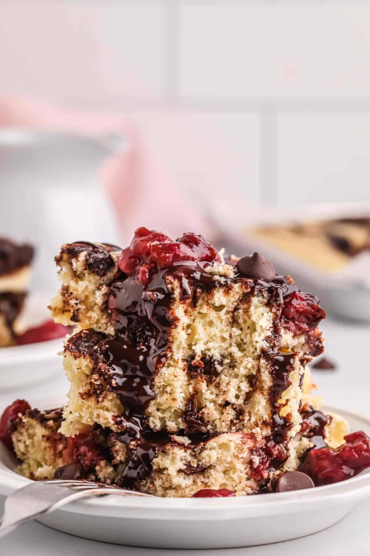 squares of chocolate cherry sheet pan pancakes stacked on top of one another in a bowl with chocolate sauce and tart cherries on top