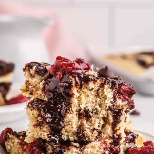 squares of chocolate cherry sheet pan pancakes stacked on top of one another in a bowl with chocolate sauce and tart cherries on top