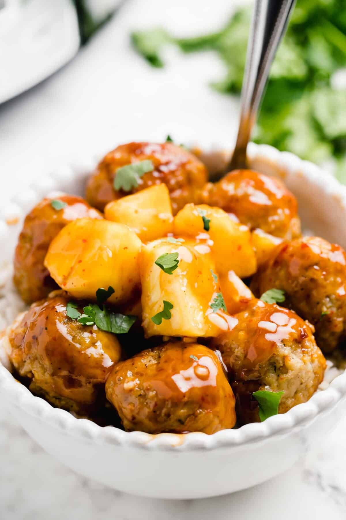 sweet and sour meatballs coated in sauce with fresh parsley on top in a white bowl