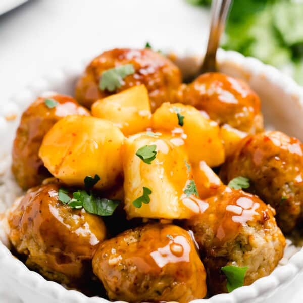 sweet and sour meatballs coated in sauce with fresh parsley on top in a white bowl
