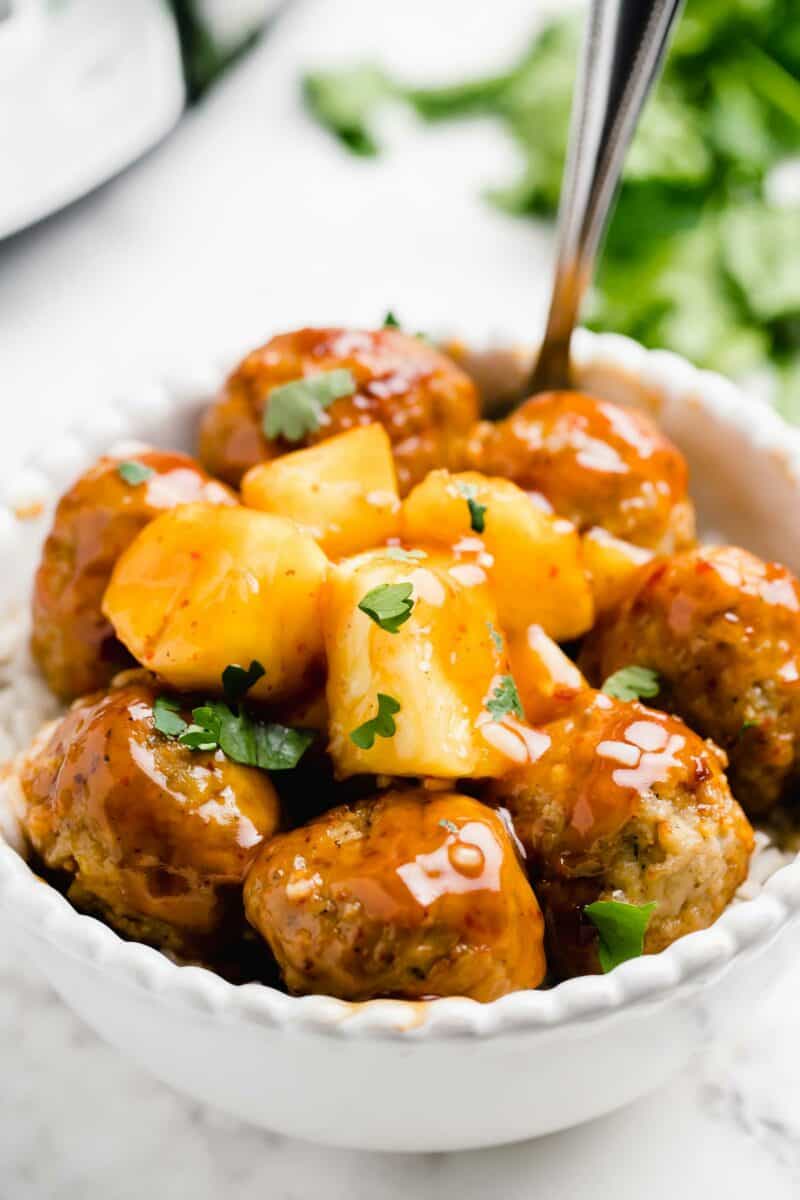 Pineapple and cilantro garnish a bowl of sweet and sour meatballs on a bed of white rice.