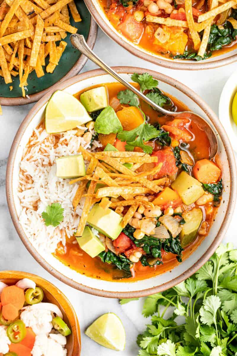 A spoon is sitting on the side of a bowl of Mexican vegetable and bean tortilla soup. 