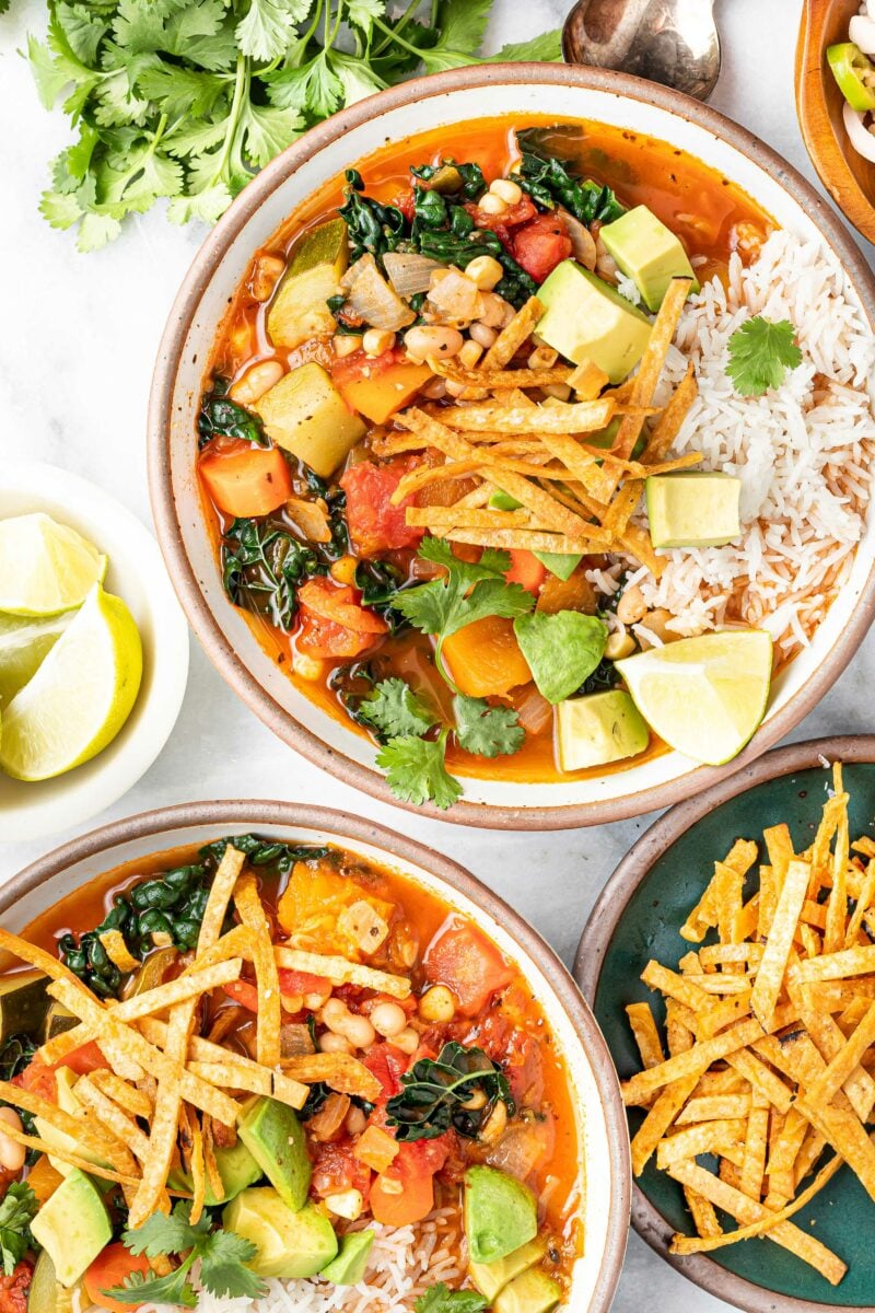 Two full bowls of soup are sitting next to each other with tortilla strips and lime on the side. 