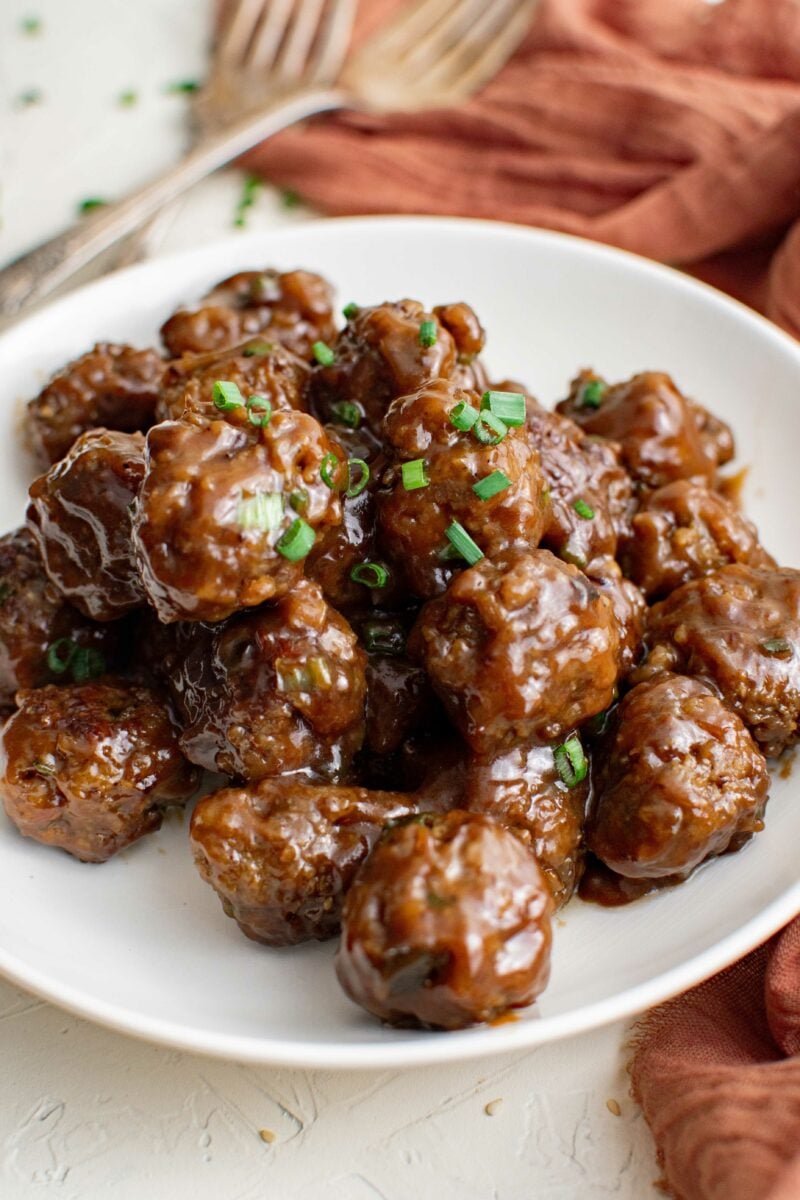 Meatballs are garnished with chopped green onions on a white plate. 