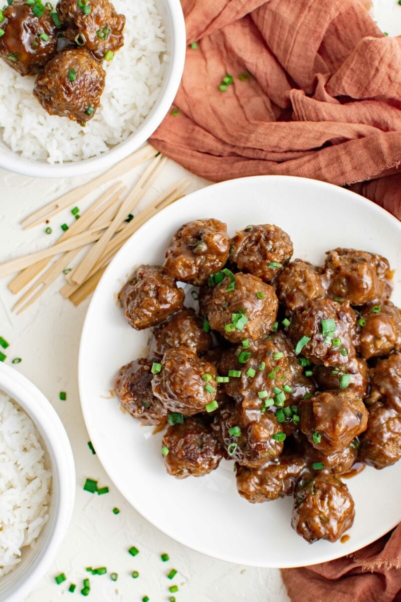 One large plate of garnished meatballs is placed next to serving picks and a small bowl of white rice and meatballs. 