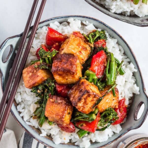 Two bowls of white rice and tofu stir fry are placed on a white surface and are ready to be eaten.