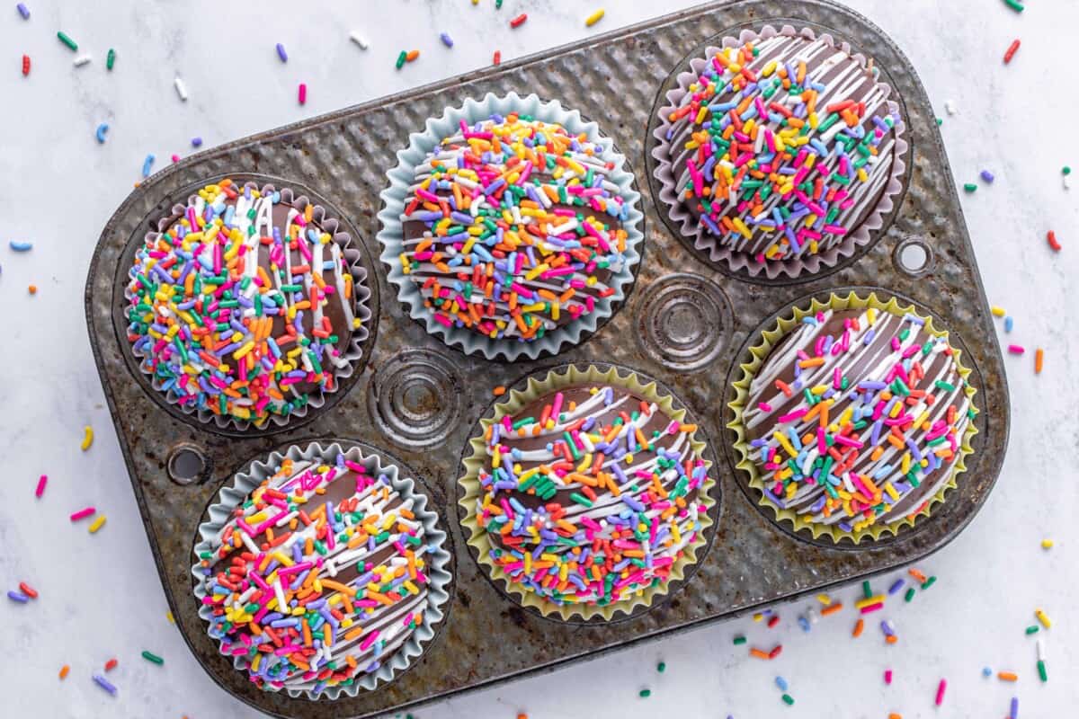 Six funfetti cocoa bombs are placed in a metal tray. 