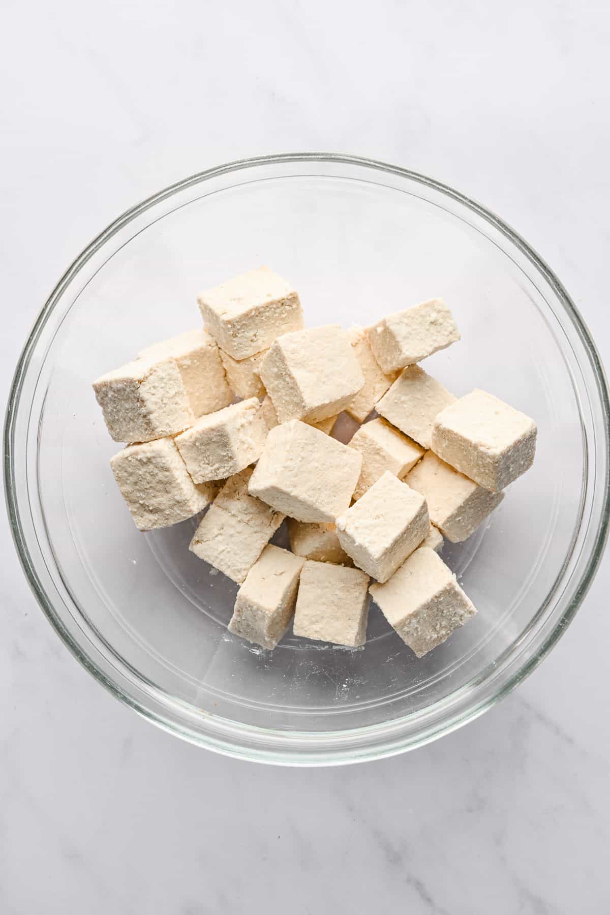 Cubed tofu coated with cornstarch in a glass bowl.
