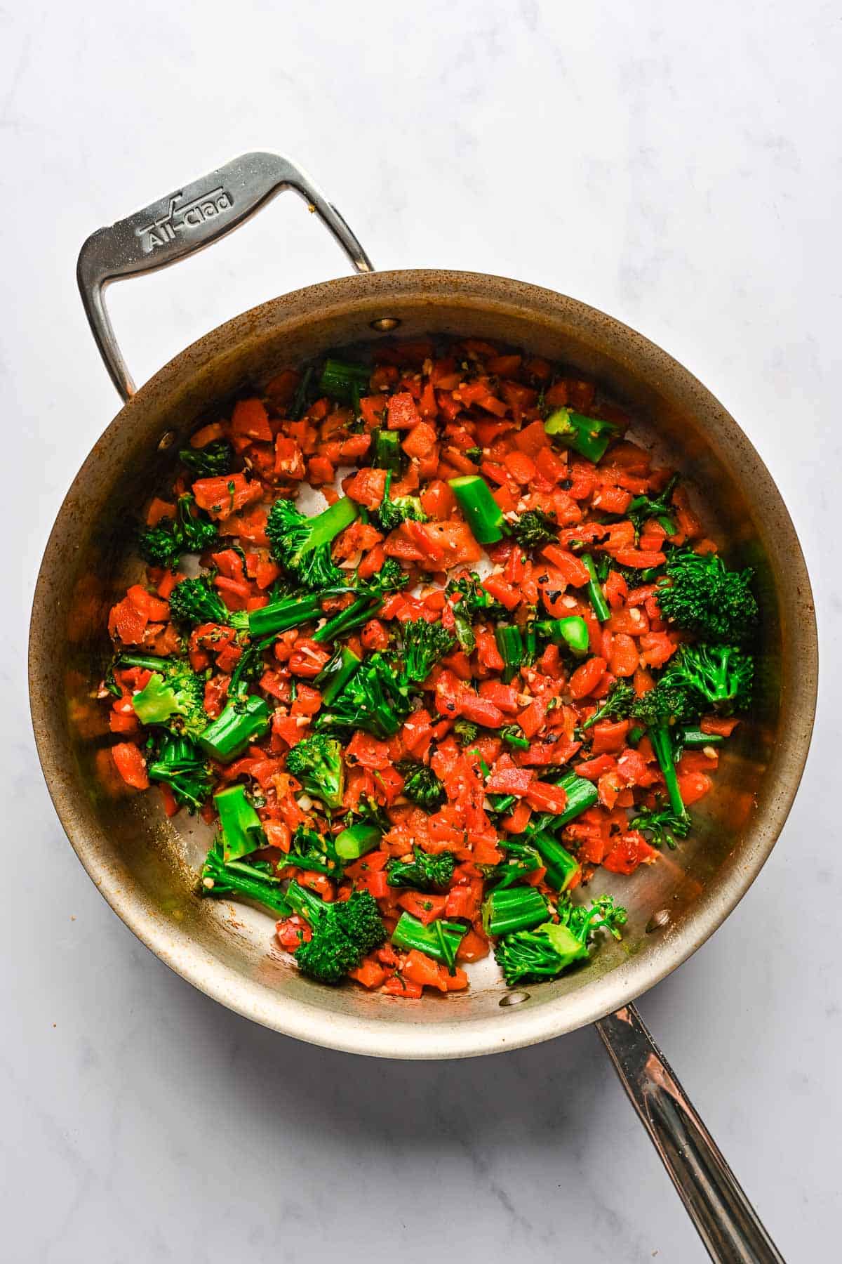 Diced roasted red peppers and broccolini in a large metal skillet.