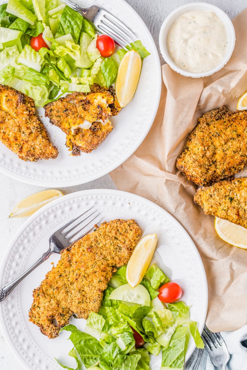 Two white plates contain servings of catfish and side salad.