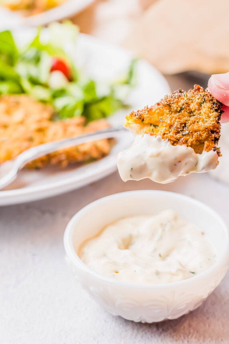 A piece of catfish is dipped into tartar sauce.