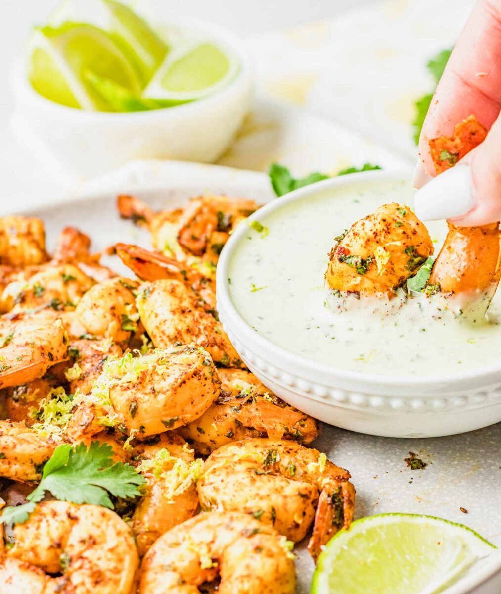 A shrimp is being dunked into a bowl of dressing. 