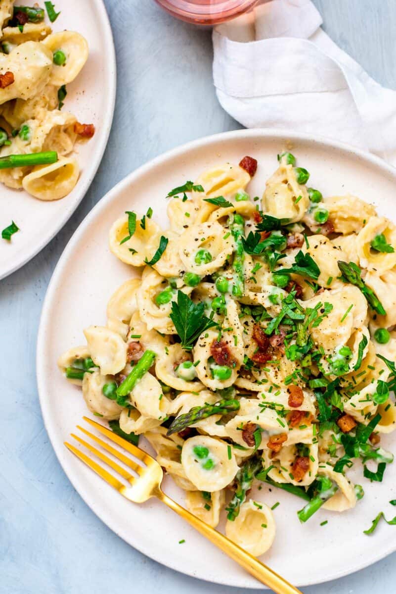 A golden fork is placed on a full plate of creamy pasta. 