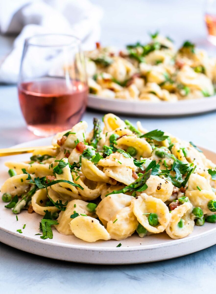 A glass of rosé is pictured in the background of a full plate of pasta. 
