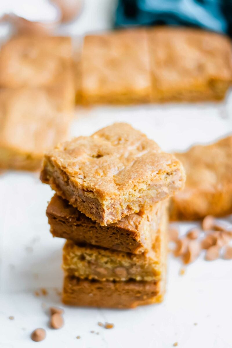 Four blondies are stacked on top of one another on a white surface. 