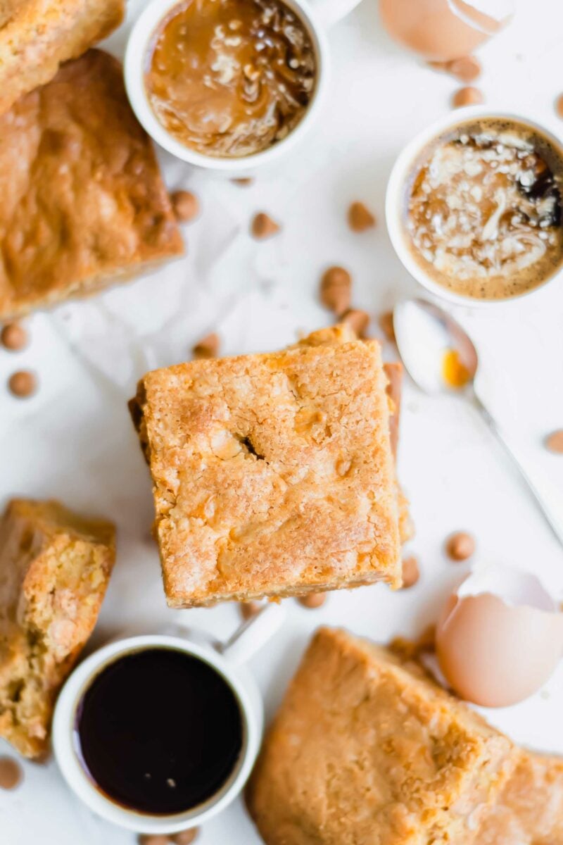 Three cups of coffee are placed next to a few pieces of blondies. 