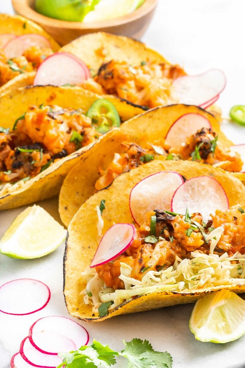 Slices of limes are placed next to cauliflower tinga tacos. 